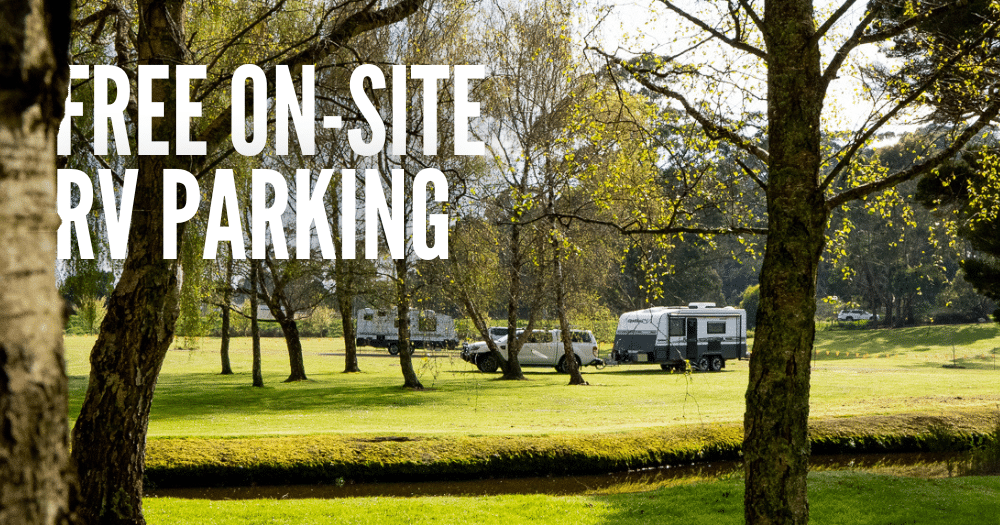 Text overlay of 'Free on-site RV parking' ontop of image of vehicles parked on a flat and very green expanse of land with trees and stream in foreground
