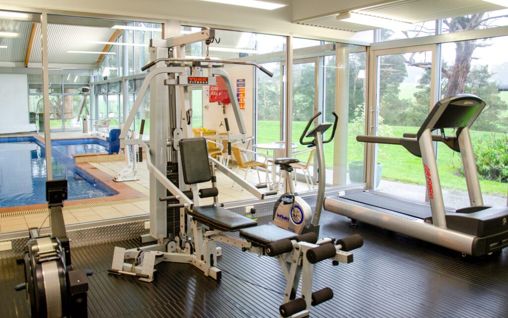 View of rowing, weights, cycling and treadmill machines in gym with view through to pool and spa