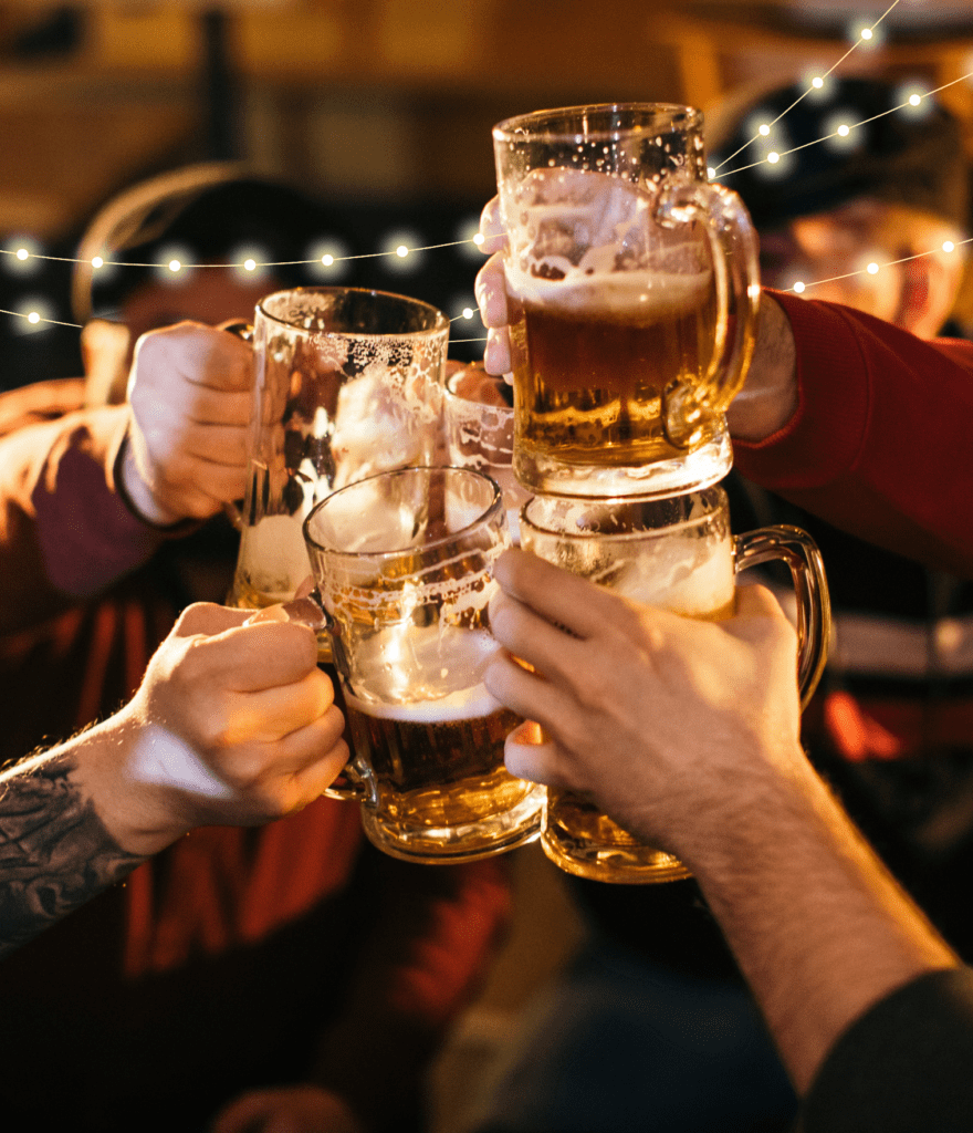 Five people clinking glasses half filled with beer in a cheers with fairy lights in background