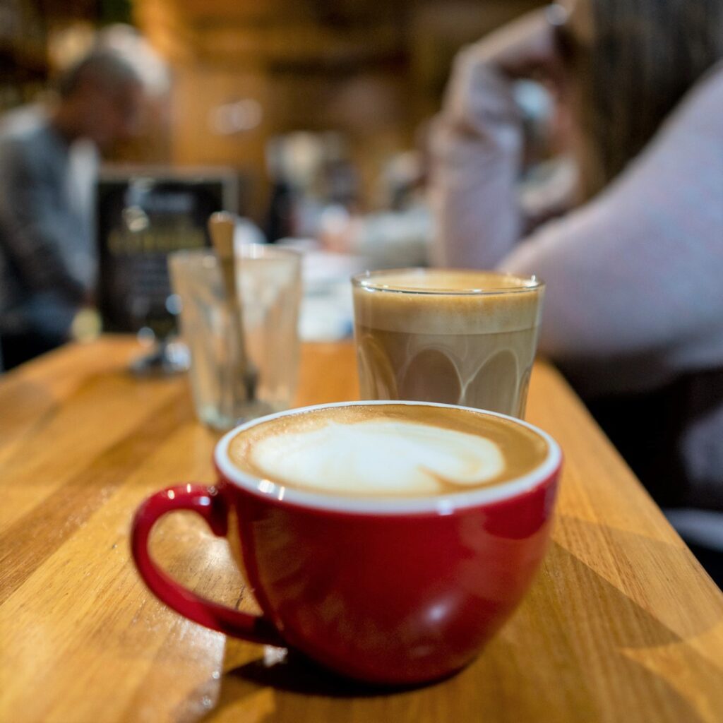 Coffee in mug and coffee in short glass on bar with people blurred in background