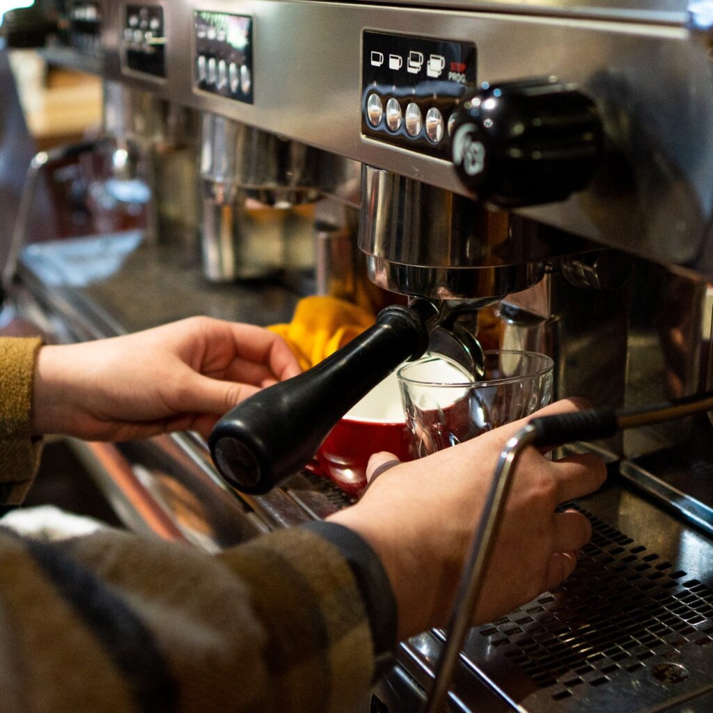 Hands of coffee making student with mug and glass under coffee pour