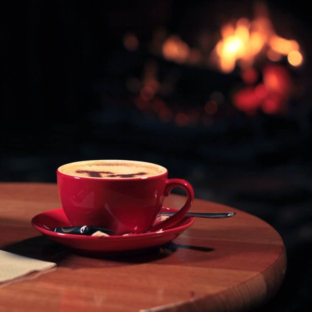 Cappuccino in red mug, on saucer in front of fire