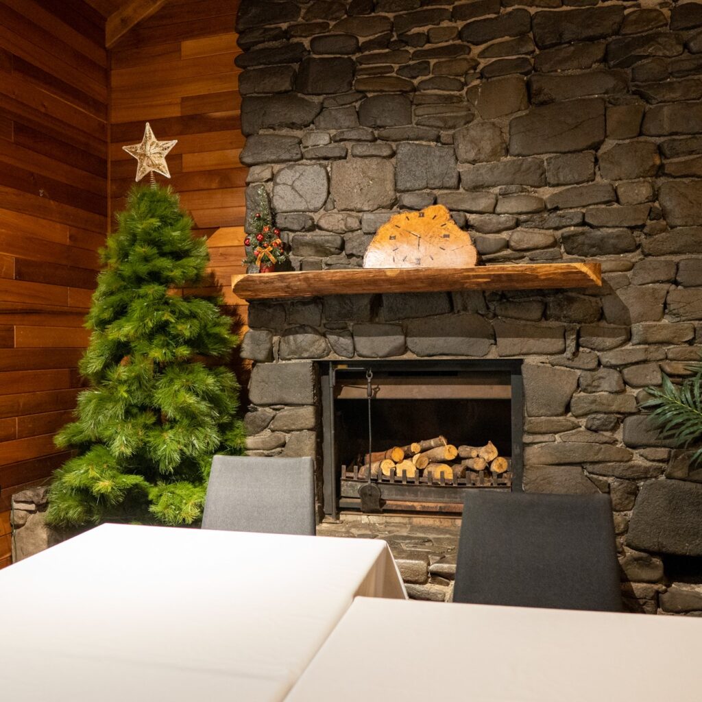 Christmas tree in corner of small function room with clock above unlit fireplace with tables in foreground