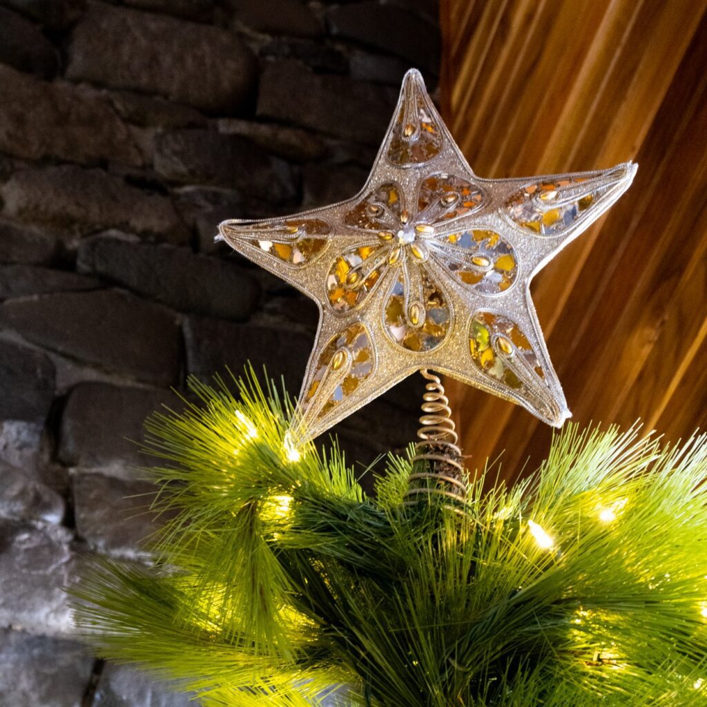 White and gold star on top of Christmas tree with join of stone wall and wood panelled wall in background