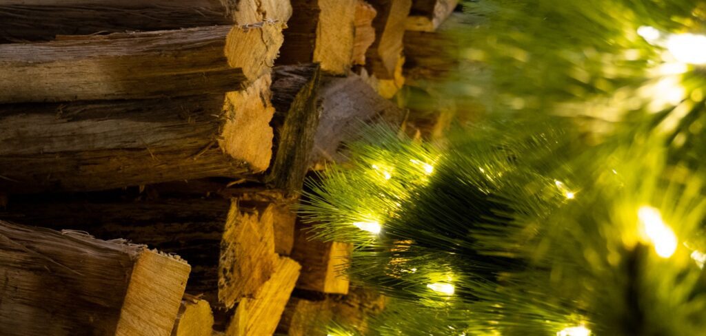 Stacked fire wood in focus background, with lit Christmas tree out of focus in foreground