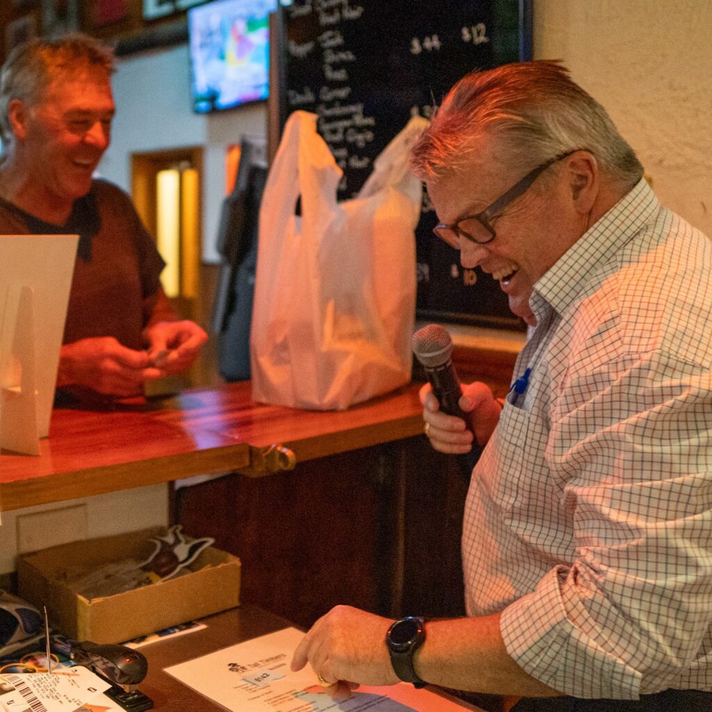 John Dabner holding microphone and giving a local their winnings