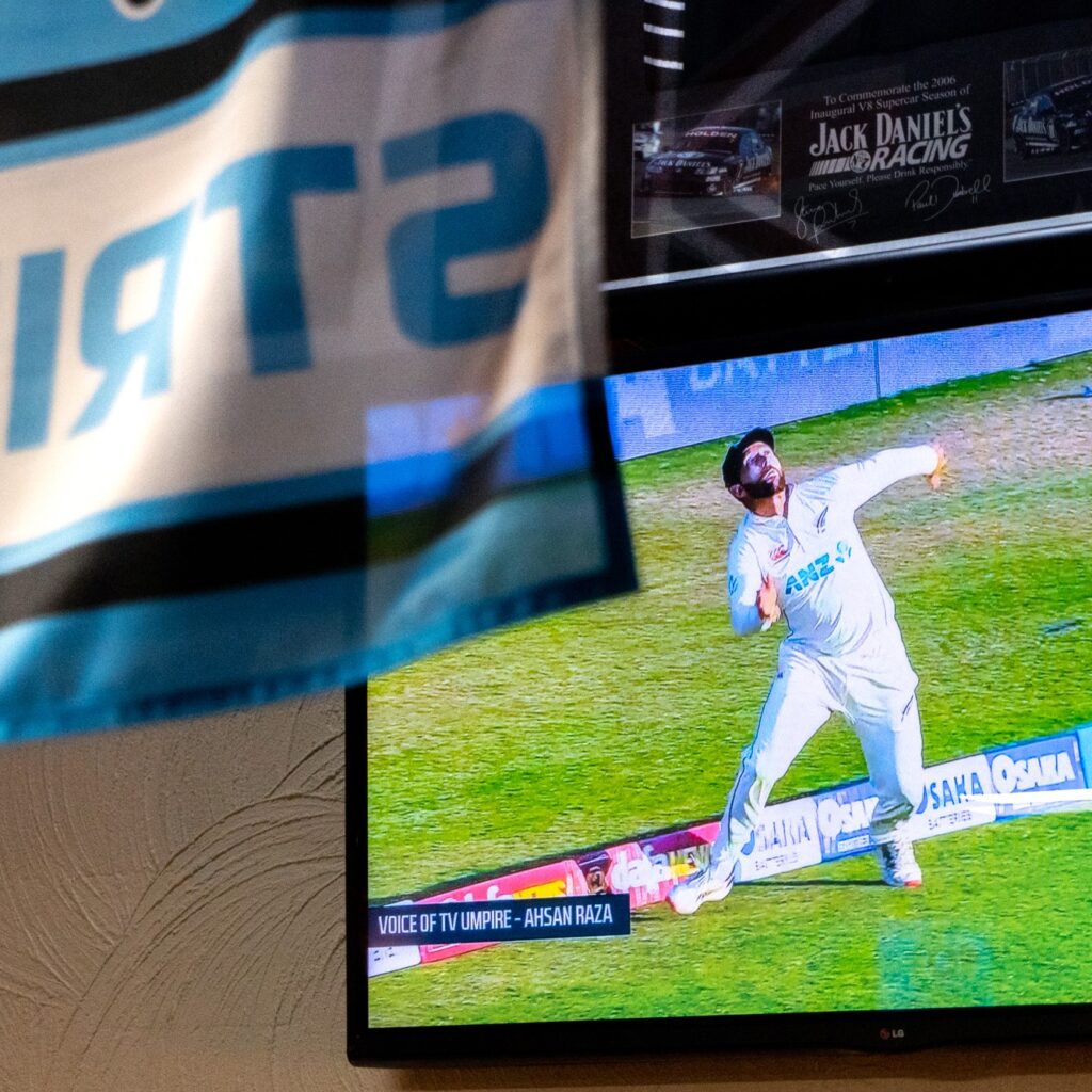 Cricket playing on television with cricket banner hanging in foreground