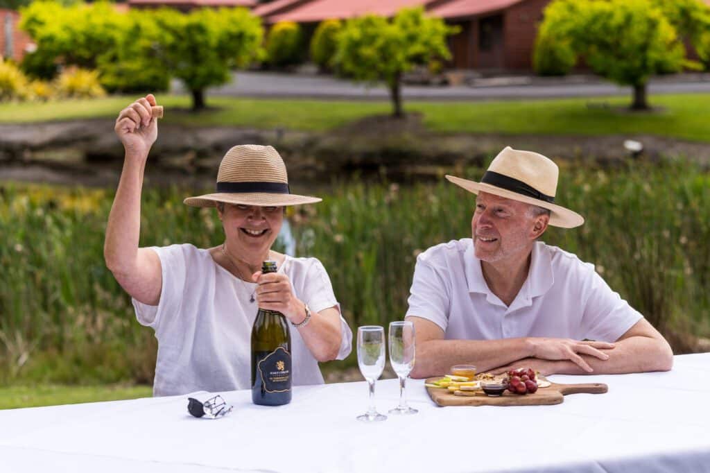 A female popping a bottle of sparkling wine with her male companion beside her